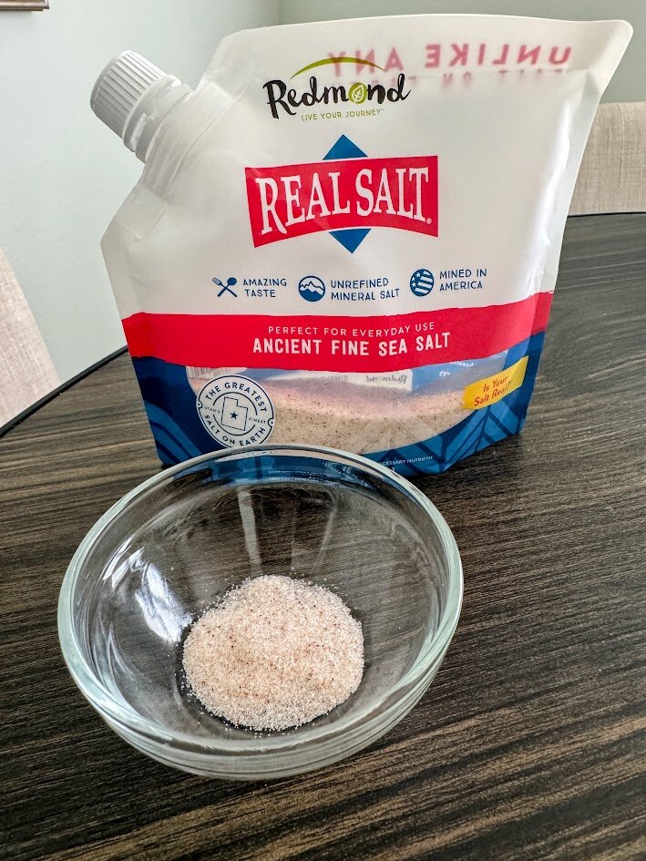 A pouch of Redmond Real Salt Ancient Fine Sea Salt behind a small glass dish of the salt